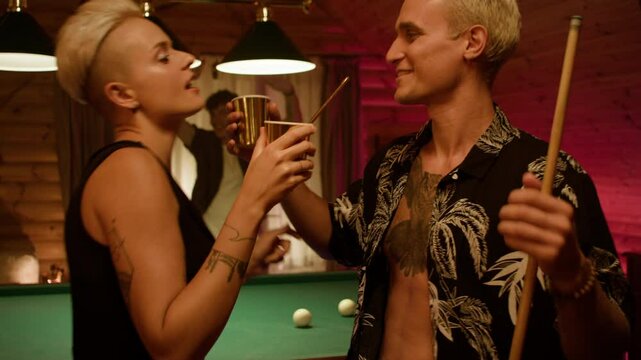 In the foreground man in black and woman in red top with white shorts kiss while holding cups. Behind a woman in black dress dances with a man in a floral shirt as a red friend watches with a drink.