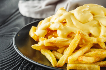 delicious crispy golden french fries with cheese on a black wooden rustic background
