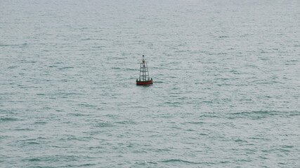Small red navigational buoy with light on top and solar panels for charging surrounded with calm blue sea on warm spring day