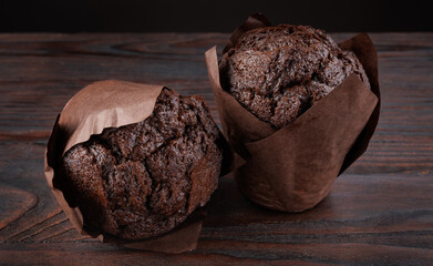 Two chocolate muffins on a wooden surface. Muffin in a paper cup.