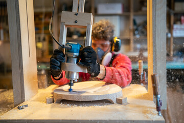 Carpenter in noise canceling headphones and respirator shaping stool base on drilling cnc machine...