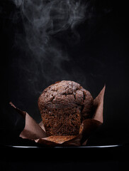Chocolate muffin in an unfolded paper cup on a dark background. Steam comes out of a fresh chocolate muffin.