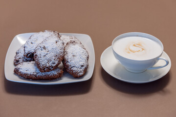 Pan dei Morti cookies dusted with powdered sugar served on a white plate with a cup of frothy cappuccino in soft, warm tones