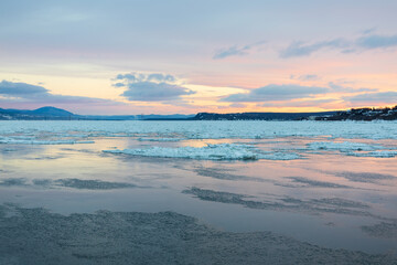 Scenic pastel winter sunrise view of the partly frozen St. Lawrence river with the Island of Orleans bridge in the background seen from the old town, Quebec City, Quebec, Canada
