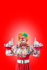 Funny clown pointing up at blank template copy spase for advertising, posters, greetings, invitations. Entertainer as Joker in a suit and wig, with clown whiteface makeup