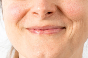 Narrow natural asymmetrical lips. Smiling mouth mimic wrinkles close up. Female face without makeup.