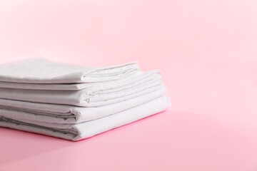 Stacked clean bed linens on pink background, space for text