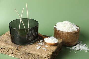 Making homemade candles. Soy wax, jar with wicks and spoon on green background