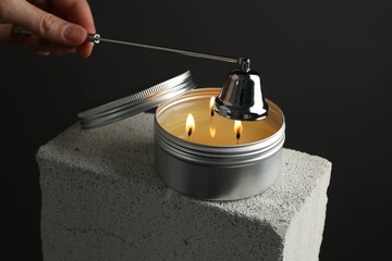 Woman extinguishing burning soy wax candle with snuffer against gray background, closeup