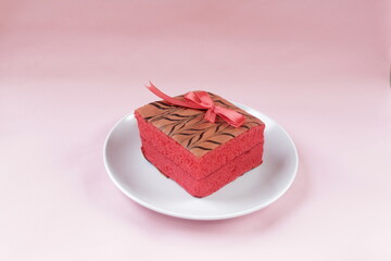 A Delicious Red Cake with A Red Ribbon on A White Plate on Pink Background