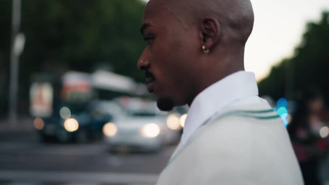 Young stylish man crossing road in evening cityscape, illuminated by car headlights and streetlights. His confident stride and focused gaze create dynamic urban atmosphere, reflecting modern lifestyle