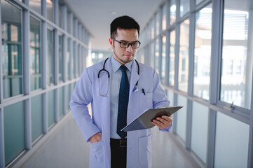 Fototapeta premium A male doctor is standing checking a list of patients in a hospital corridor.