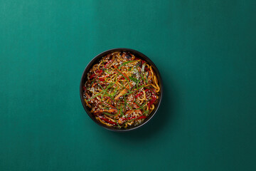 top shot on green background black salad plate with Chinese noodles noodles with veal slices Asian cuisine healthy eating sprinkled with sesame seeds