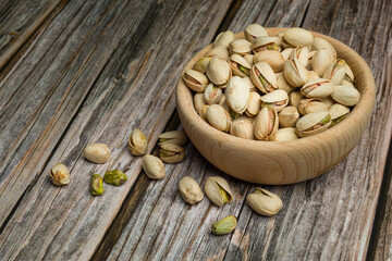 Bunch of pistachio nuts on wooden bowl on wooden table.