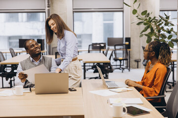 Professional team brainstorming, sharing laptops and documents in contemporary workspace, highlighting collaborative corporate culture
