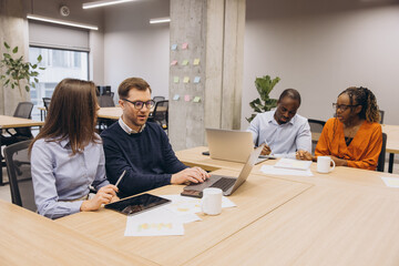 Four colleagues working together on a project, using laptops and tablets, sharing ideas and strategies in a bright open space
