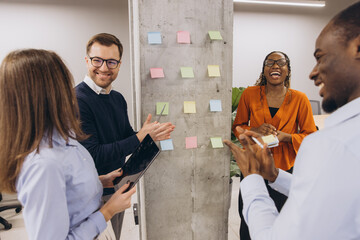 Diverse businesspeople discussing new project ideas using sticky notes on a wall in a modern office
