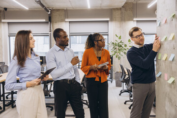 Business team collaborating on a project, using sticky notes on a wall in a modern office