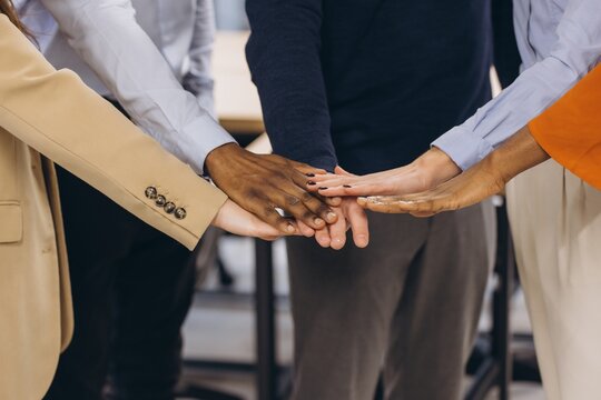 Business team joining hands in a modern office, demonstrating unity, collaboration, and teamwork among diverse professionals