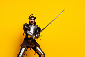 Young man in medieval knight armor holding sword on vibrant yellow background