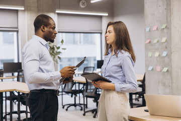 Fototapeta premium Businessman and businesswoman engaging in a work discussion in a modern office, utilizing a tablet and clipboard for effective collaboration
