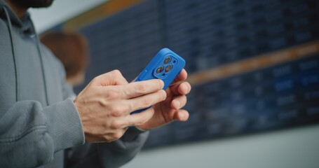 International Airport Terminal: Man Using Smartphone to Check Information for Boarding Plane Flight. Rack Focus on Digital Arrival and Departure Information Screen. Tourist Going on Vacation Trip.