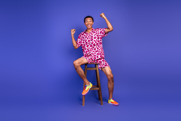 Vibrant young man celebrating in stylish pink leopard print outfit on purple background, exuding confidence and charm