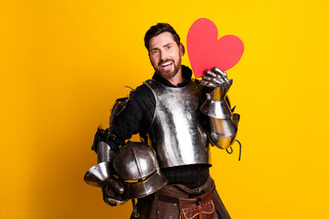Naklejka premium Man in medieval knight armor holding a heart prop on bright yellow background