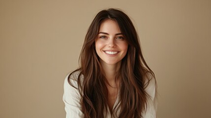 Fototapeta premium Smiling Caucasian woman with long brown hair wearing white sweater against beige background, exuding happiness and warmth in a studio setting.