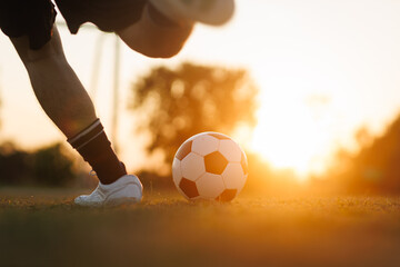 Soccer player with a ball. Action sport outdoors playing football for exercise at green grass field under the twilight sunset.