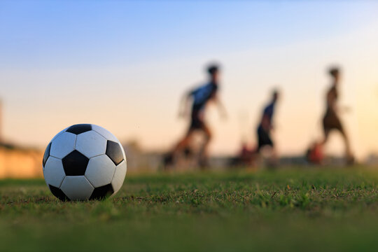 Fototapeta Action sport outdoors of kids having fun playing soccer football for exercise in community rural area under the twilight sunset sky.