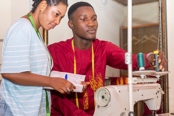 Young female trainee African-American ethnicity, learning craft from a male tailor