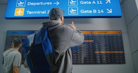 Airport Terminal: Man with Backpack Checks Flight Information Scanning Ticket Using Phone, Looks at...