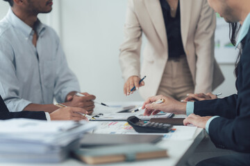 Strategic Collaboration: A diverse team of professionals leans over a conference table, engrossed in a detailed discussion, examining charts and data.