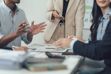 Business Meeting Collaboration: A diverse team of professionals engages in a collaborative business meeting, actively participating in a discussion around a table filled with documents and technology.