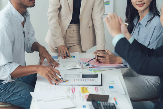 Business Team Meeting: A diverse group of professionals collaborates around a table strewn with financial documents and reports, engaging in a lively discussion and strategic planning session.   - Powered by Adobe