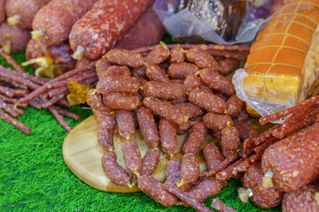 A variety of meats and sausages are displayed on a wooden cutting board. The meats include hot dogs, salami, and other types of sausage.