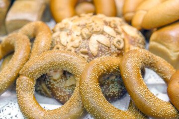 A variety of breads and rolls are displayed on a table. The breads are of different shapes and sizes, and some of them have sesame seeds on them.