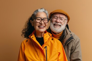Portrait of a joyful mixed race couple in their 60s sporting a waterproof rain jacket isolated on pastel brown background