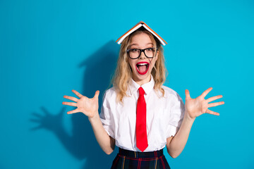 Excited schoolgirl with a book on her head striking a playful pose in a colorful background