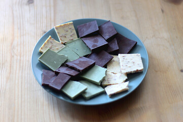 Plate with dark, white and matcha chocolate pieces. Selective focus, wooden background.