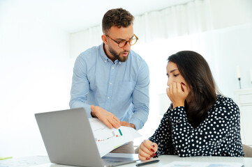 Misunderstanding between coworkers. A worried man in glasses and a blue shirt shows financial chart to his female colleague, both looking at a graph with concerned expressions, analyzing reports