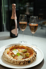 A delicious pizza with a variety of toppings, served with a glass of pink wine. Meal for a romantic dinner