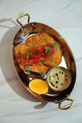 A top-down view of breaded cutlet, topped with a tomato salad and served with a side of sauce