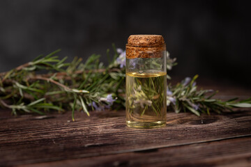 Rosemary essential oil in a glass bottle with cork lid on rustic wooden table