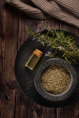 Rosemary essential oil and dried sprigs on rustic wooden table