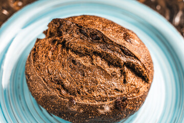 A loaf of rye bread on a turquoise or blue plate on a brown background. Close-up. Top view, Space for text