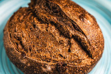 A loaf of rye bread on a turquoise or blue plate on a brown background. Close-up. Top view, Space for text