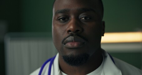 Young African doctor, dressed in a white coat with a stethoscope, gives a serious look.