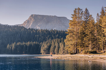 Tourist walking along the shore of the Black Lake enjoying the picturesque view of the Durmitor massif in Montenegro National Park